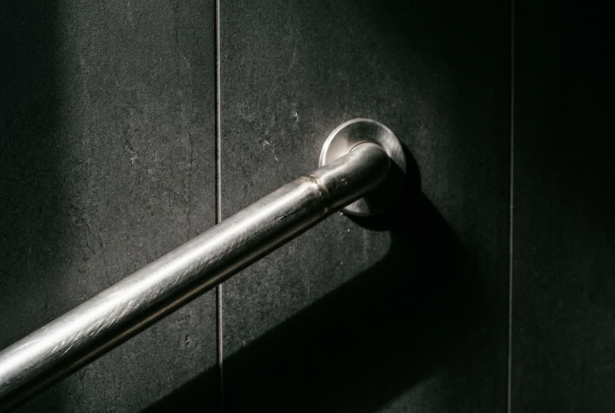 A brushed stainless steel grab bar mounted on dark grey bathroom tile